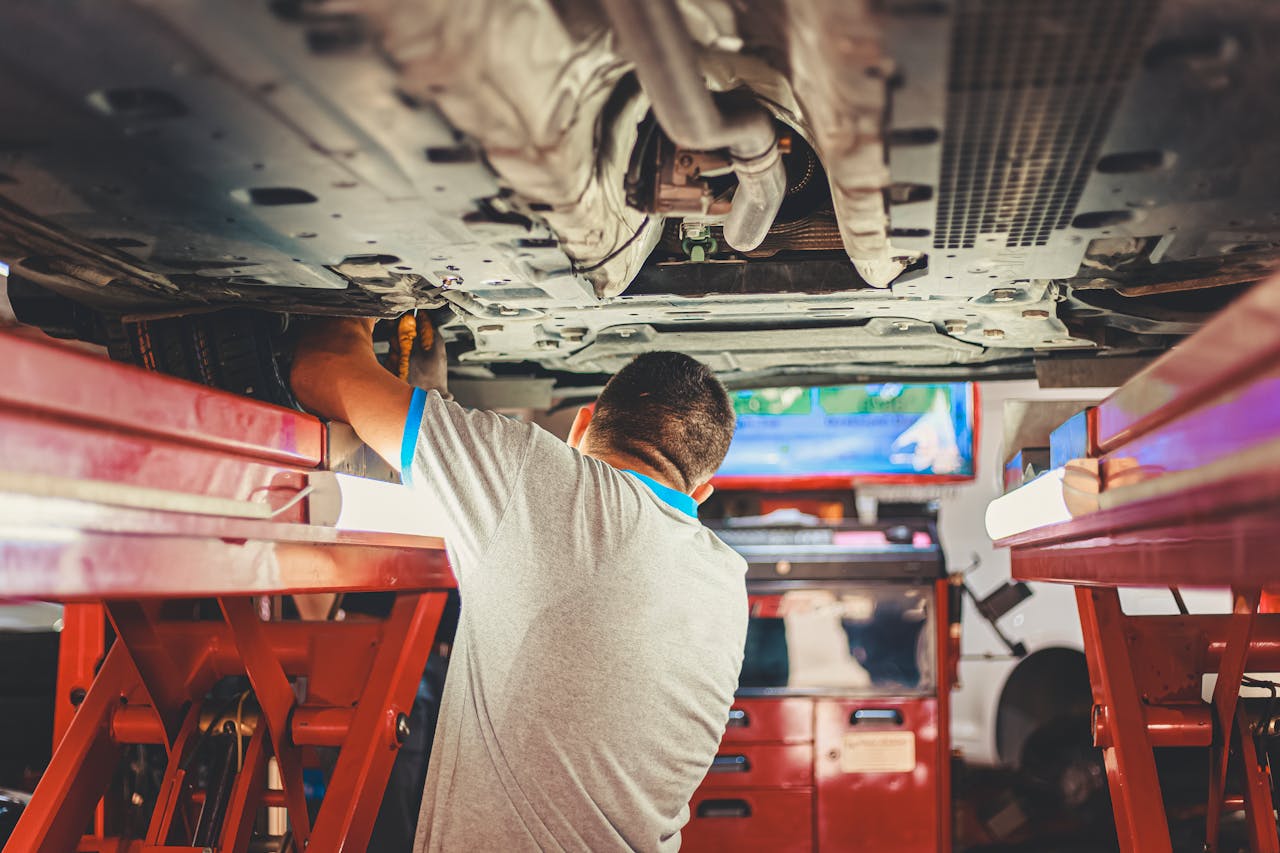 A mechanic works under a lifted car in an auto repair shop, adjusting parts.
